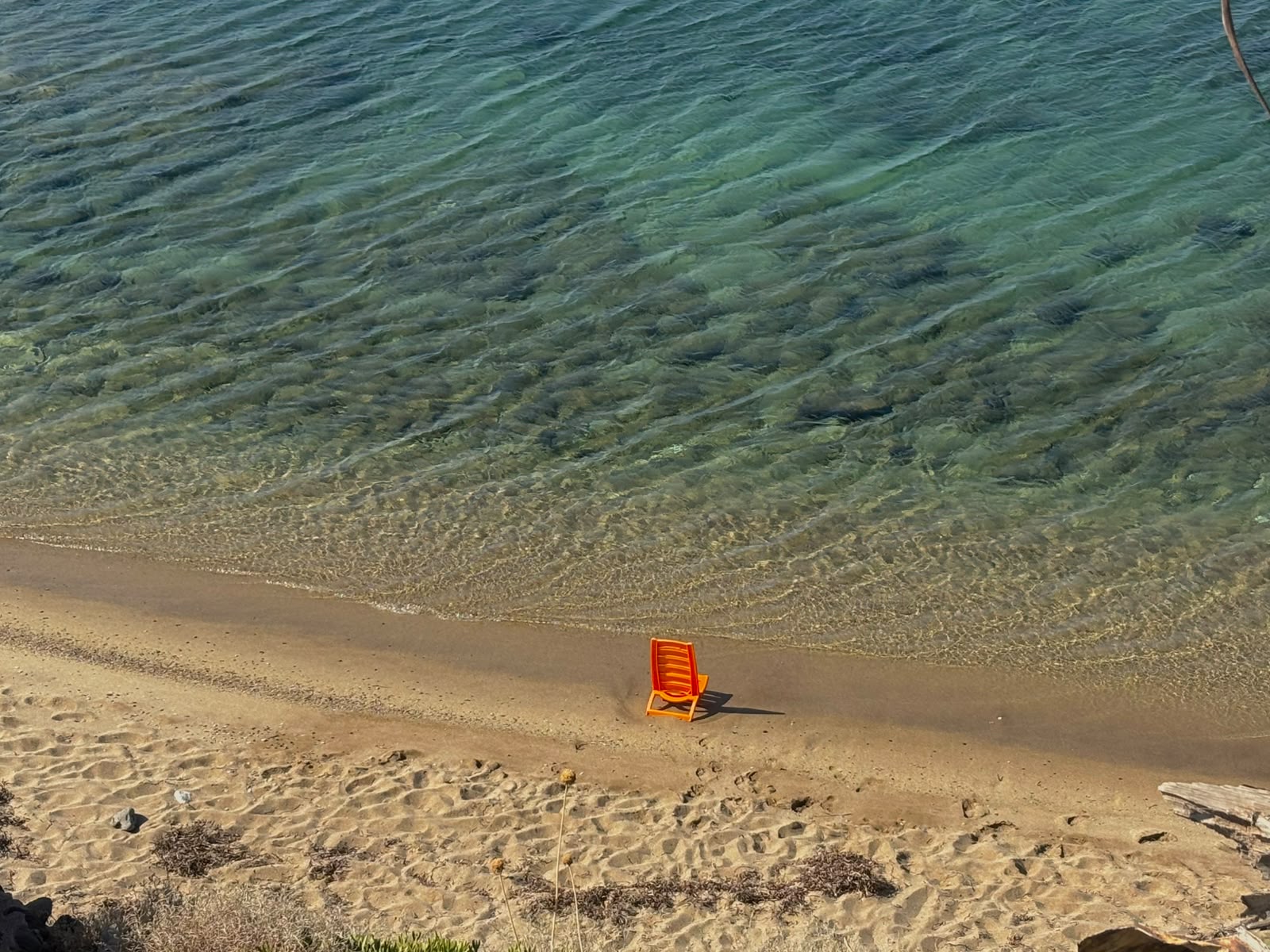 Fotografie von Anika Yago – Orangefarbener Strandstuhl am Wasser