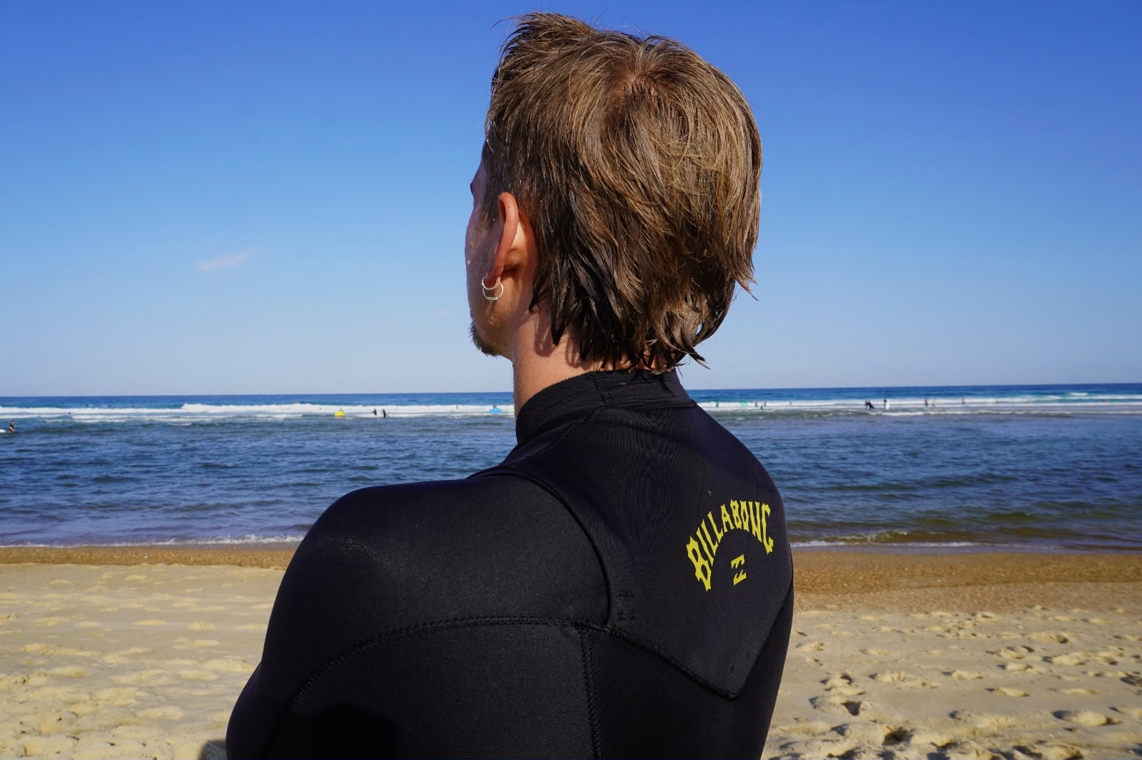 Fotografie von Anika Yago – Surferin im Neoprenanzug blickt auf die Wellen